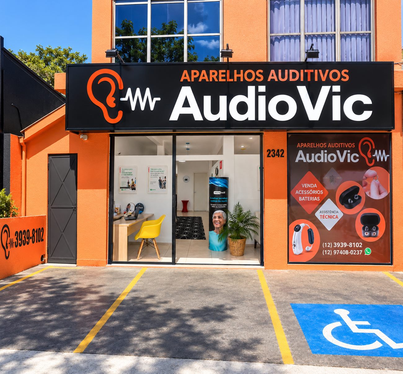 Fachada frontal da AudioVic: prédio laranja, placa preta com o nome da loja e vitrine adesivada